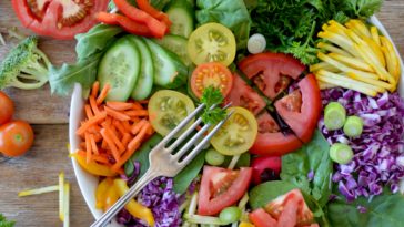 Salatschlüssel auf einem Holztisch mit und umgeben von gleichmäßig geschnittenem Gemüse
