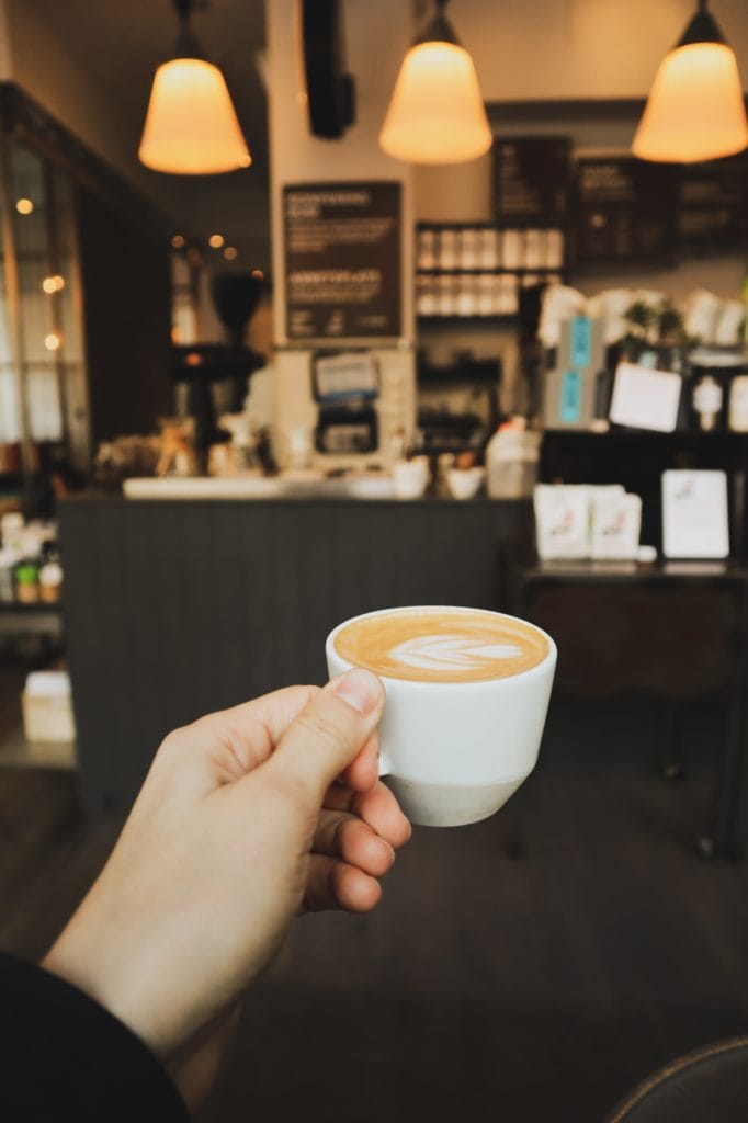 Frau hält Kaffeetasse mit Cappucchino in einem Café