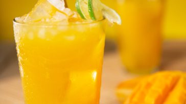 Mangosaft mit Zitrone und Eiswürfeln im Gas auf einem Tisch mit Mangos und Zitronen